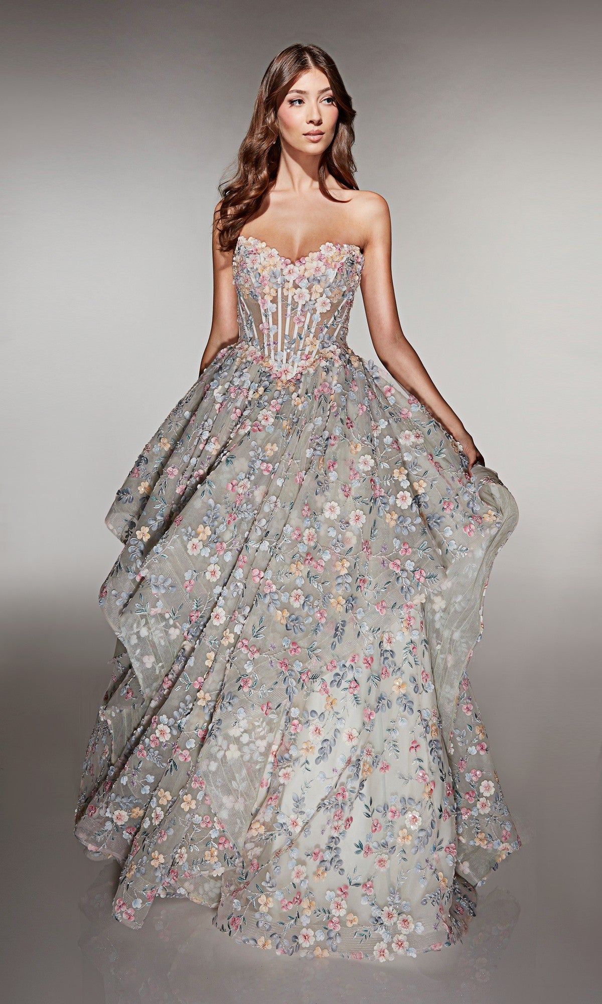 A woman wearing the Alyce 62048 long prom dress, a strapless ball gown with a sheer corset bodice and a full skirt decorated with multicolored floral applique embroidery.